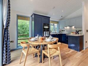 A modern kitchen with a round dining table, wooden chairs, and a view of greenery outside. - 2 Bed in Truro (oc-93311) (Porthtowan)