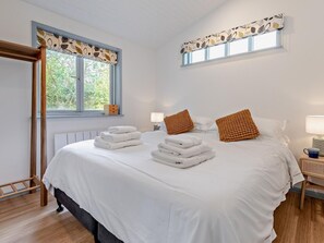 Une chambre d’hôtel avec un lit, deux tables de chevet, une fenêtre agrémentée d’un lambrequin à motifs de feuilles et une vue sur la verdure environnante.