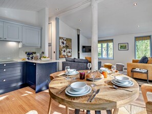 A modern kitchen with a central island, a dining area with a round wooden table, and a living space with sofas and a large window.