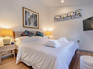 A hotel room with a bed, two bedside lamps, a flat-screen TV, and artwork on the walls.