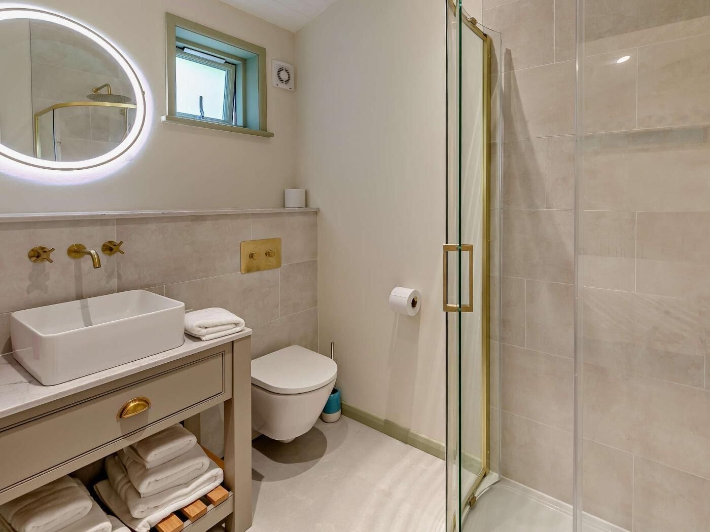 A bathroom with a glass-enclosed shower, a white sink with gold fixtures, a toilet, and a mirror with a light.