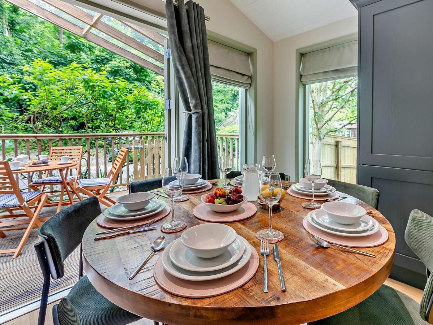 A round dining table set for six with plates, glasses, and cutlery, overlooking a lush garden.