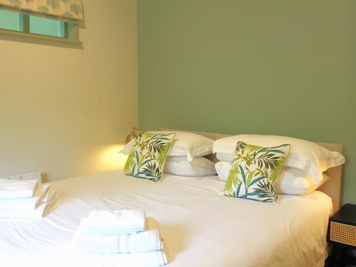 A neatly made bed with white linens and two decorative pillows with a tropical leaf pattern.