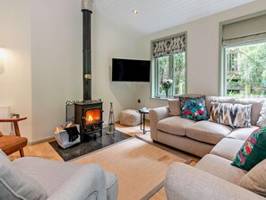 Ein Wohnzimmer mit Kamin, einer Couch, einem Fernseher und einem Fenster mit Blick auf Grünflächen.