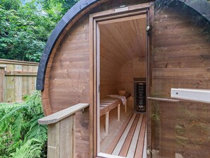 A wooden sauna with a bench and a bench seat, surrounded by a wooden deck and greenery.