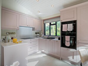 Eine moderne Küche mit rosa Schränken, einem Edelstahl-Kühlschrank und einem Fenster mit Blick auf Grünflächen.