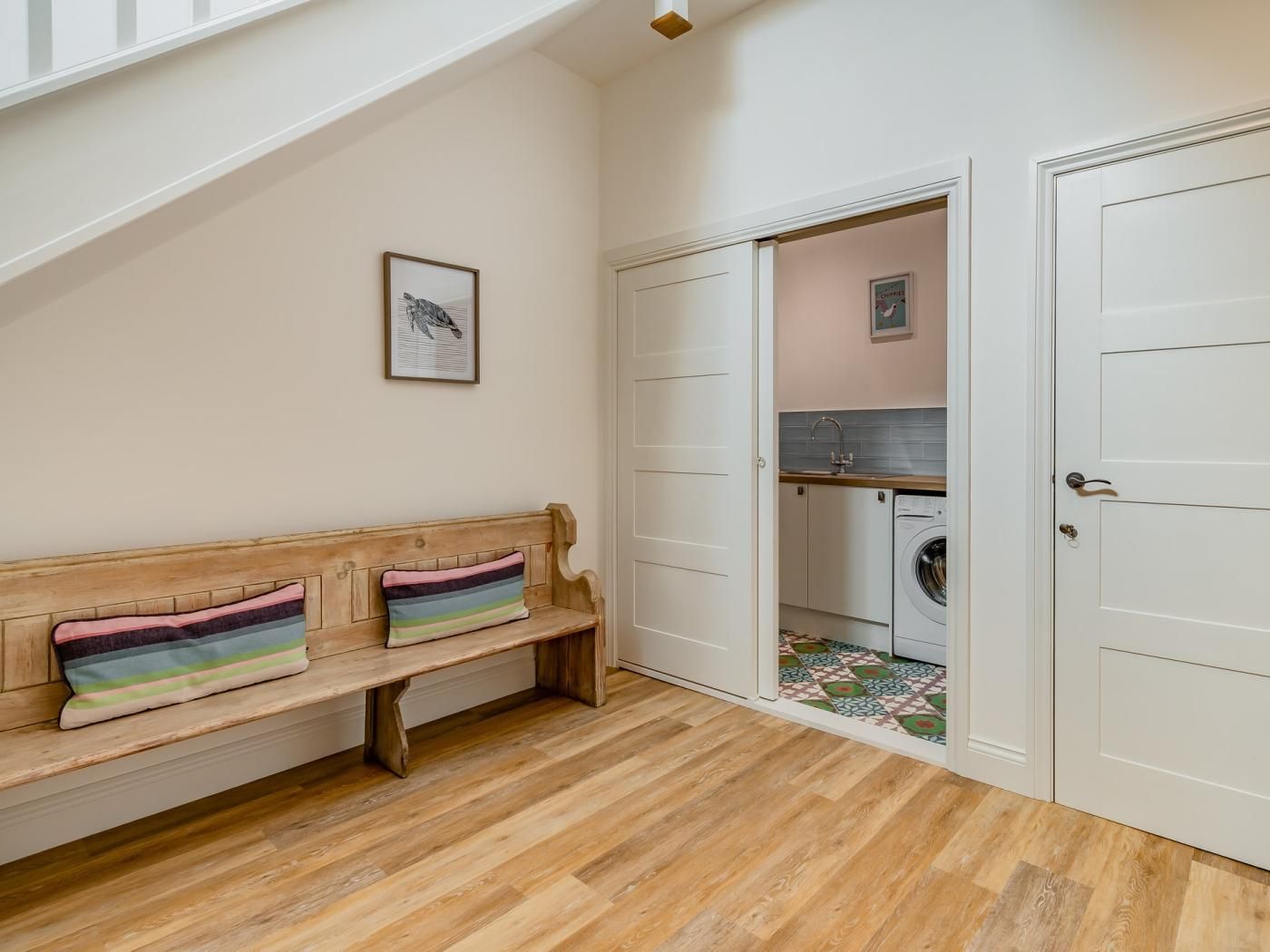 A room with a wooden bench, a door leading to a laundry area, and a framed picture on the wall.