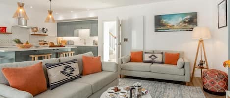 A modern living room with a grey sofa, a coffee table, and a kitchen in the background.