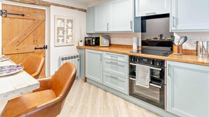Eine moderne Küche mit hellblauen Schränken, einer Holz Arbeitsplatte, einem eingebauten Ofen und einem Essbereich mit Tisch und Ledersessel.