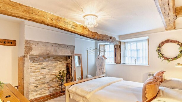 Ein Schlafzimmer mit einem Bett, einem Kamin, einem Holzbalken an der Decke, einer Kristallleuchter und einem Fenster mit Aussicht.
