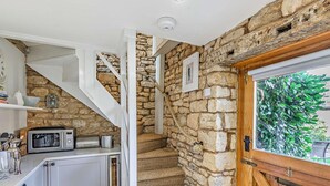 A kitchen with a microwave, toaster, and cabinets, a stone staircase, and a wooden door with a view of greenery. - 1 Bed in Chipping Campden (oc-93393) (Chipping Campden)