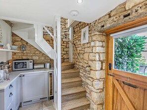 Eine Küche mit Mikrowelle, Toaster und Schränken, eine Steintreppe und eine Holztür mit Blick auf Grünflächen.