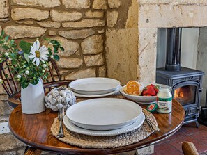 A dining table set with plates, a vase with flowers, a bowl of strawberries, a jar of cream, and a wood-burning stove. - 1 Bed in Chipping Campden (oc-93393) (Chipping Campden)