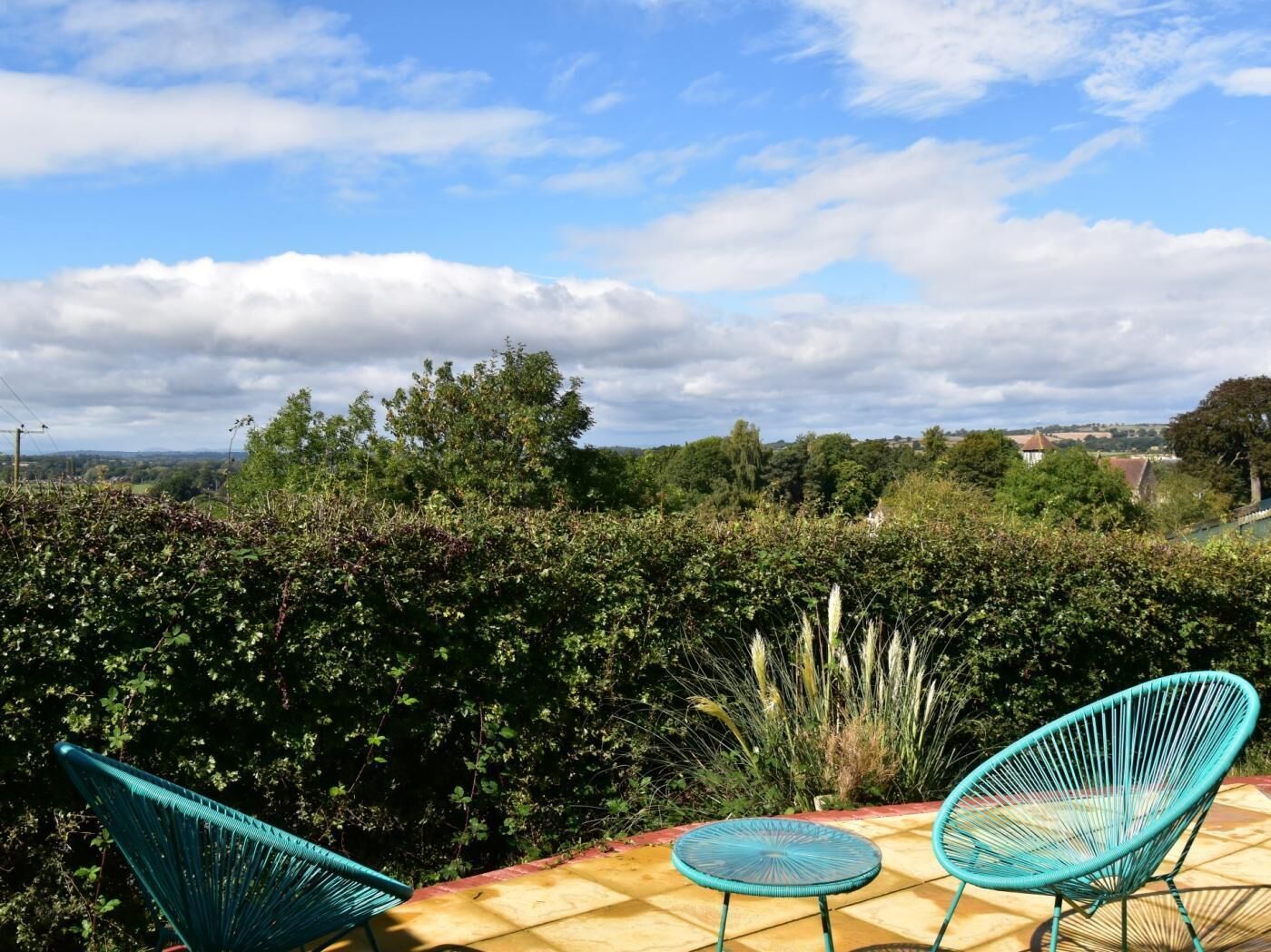 A patio with two chairs and a small table, surrounded by dense foliage and a view of a distant landscape.
