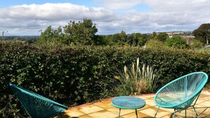 Un patio con dos sillas y una pequeña mesa, rodeado de follaje exuberante y vistas a un paisaje lejano.