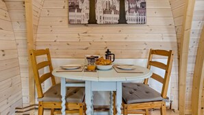 Una habitación con paneles de madera, una mesa redonda, dos sillas, una cafetera y un vaso de jugo de naranja.