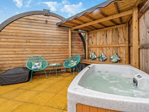 A wooden outdoor patio with a hot tub, two chairs, and a bench.