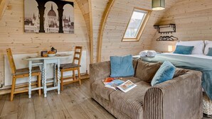 Una habitación acogedora con techo de madera, una mesa de comedor con sillas, un sofá con revistas y una cama con almohadas.