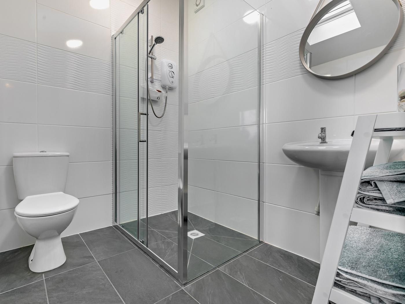 A modern bathroom with a glass-enclosed shower, a white toilet, a sink, and a mirror.