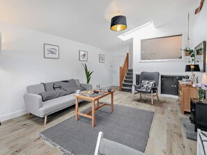 A modern living room with a grey sofa, a coffee table, a black and white rug, a wooden chair, and a fireplace. - 1 Bed in Penzance (oc-93410) (Sennen)