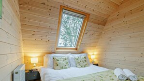 Ein Schlafzimmer einer Holzhütte mit Bett, Kissen, einem Nachttisch, einer Lampe und einem Fenster.