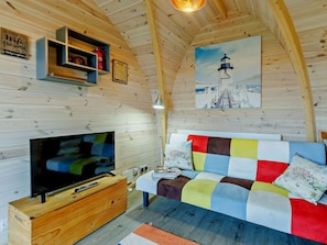 Ein gemütliches Blockhaus-Interieur mit Fernseher, einem Bett mit bunter Bettwäsche, einem Leuchtturm-Gemälde und einer Holzbalkendecke.