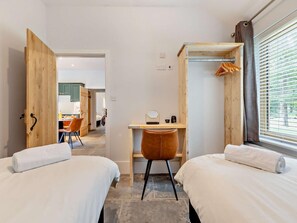 A hotel room with two beds, a desk, and a chair. There is a window with blinds and a view of greenery outside. - 3 Bed in King's Lynn (oc-93412) (Middleton)