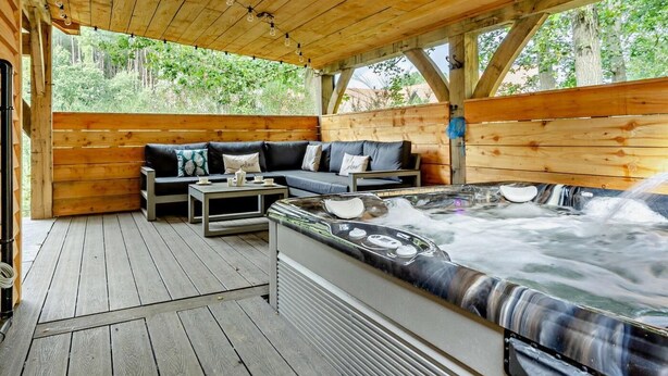 A wooden deck with a sofa, a table, and a hot tub. - 3 Bed in King's Lynn (oc-93412) (Middleton)