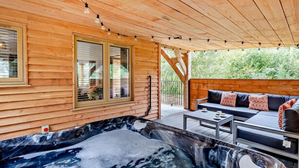 A wooden cabin with a hot tub, outdoor seating, and a window overlooking greenery. - 3 Bed in King's Lynn (oc-93413) (Middleton)