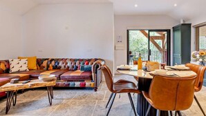 A modern living room with a leather sofa, a dining table with chairs, and a staircase leading to an upper level. - 3 Bed in King's Lynn (oc-93413) (Middleton)