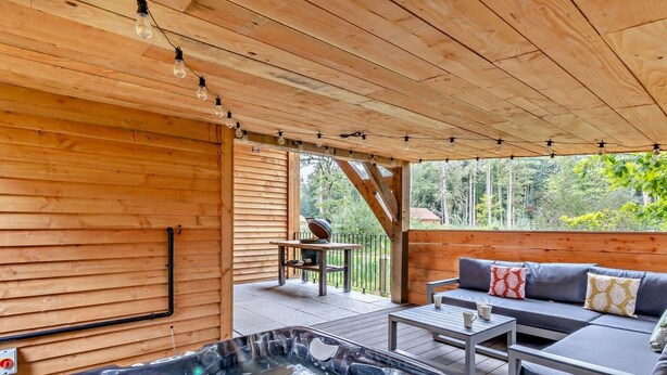 Een houten vakantiehuis met een jacuzzi, buitenmeubels en uitzicht op het bos.