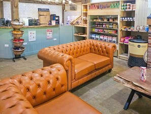 A cozy interior with a leather sofa, a coffee station, and shelves stocked with various products. - 3 Bed in King's Lynn (oc-93415) (Middleton)