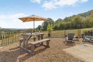 Eine Terrasse im Freien mit einem Holztisch und Bänken, einem Picknicktisch und einem großen Sonnenschirm.