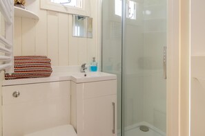 Ein Badezimmer mit Duschkabine aus Glas, einem weißen Waschbecken und einem Spiegel darüber.