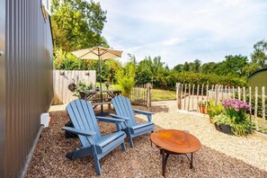 A patio area with Adirondack chairs, a table, and a round table with a cushion. - 1 Bed in Hereford (oc-93441) (Little Dewchurch)
