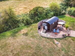 Ein einstöckiges, gebogenes Holzgebäude mit einem eingezäunten Patio, einer kleinen Terrasse und einem überdachten Sitzbereich im Freien.