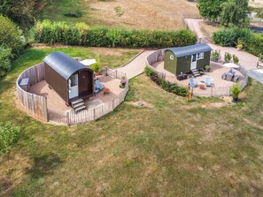 Un espace extérieur clos, comprenant deux petites constructions : l’une avec un toit incurvé et l’autre avec un toit plat, le tout entouré de pelouse et d’un chemin de gravier.