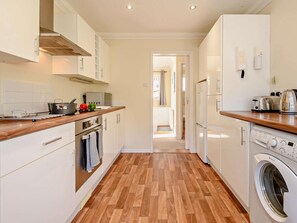 A modern kitchen with wooden flooring, white cabinetry, a built-in oven, and a washing machine. - 3 Bed in Christchurch (oc-93459) (Christchurch)