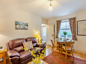 A living room with a brown leather sofa, a dining table with chairs, a lamp, and a window with curtains. - 2 Bed in Penrith (oc-93492) (Glenridding)