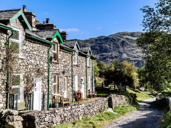 A stone building with a green roof, a stone wall, and a gravel path leading to it. - 2 Bed in Penrith (oc-93492) (Glenridding)