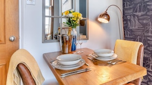A dining table set with plates, cutlery, and a champagne bottle, with a mirror and a lamp on the wall. - 1 Bed in Bridport (oc-93502) (West Bay)