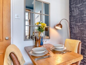 Ein Esstisch ist gedeckt mit Tellern, Besteck und einer Champagnerflasche, an der Wand befinden sich ein Spiegel und eine Lampe.