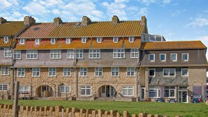 A multi-story stone building with a row of windows, a stone wall in the foreground, and a clear sky. - 1 Bed in Bridport (oc-93502) (West Bay)