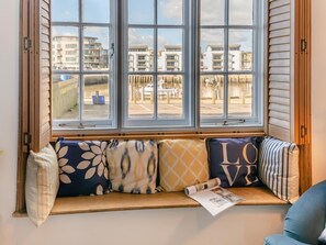 Ein Fensterplatz mit vielen Kissen und einer Zeitschrift.