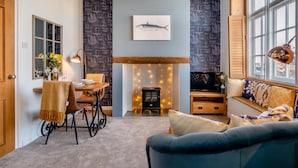 A cozy living room with a fireplace, a dining area with a table and chairs, and a large window with a view. - 1 Bed in Bridport (oc-93502) (West Bay)