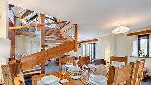 Un coin repas avec une table en bois dressée pour quatre personnes, un escalier en bois et une vue sur l’étage supérieur.