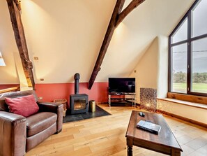A loft-style room with a fireplace, a television, a leather sofa, and a large window. - 7 Bed in Bideford (oc-93523) (Weare Giffard)