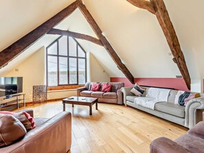 A loft-style living room with exposed wooden beams, a large window, and a modern TV. - 7 Bed in Bideford (oc-93523) (Weare Giffard)