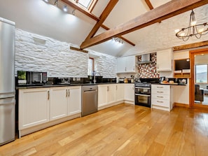 A modern kitchen with white cabinetry, a stone wall backsplash, wooden beams, and a view of the outdoors. - 3 Bed in Keswick (oc-93590) (Threlkeld)