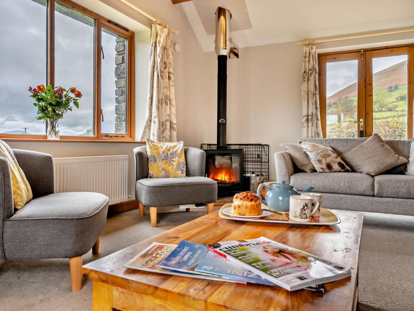 A cozy living room with a fireplace, comfortable seating, and a view through large windows.